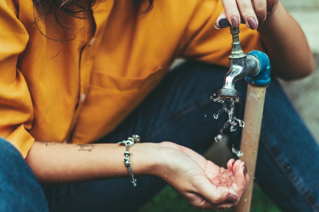 person-opening-faucet-and-washing-own-hands-1854868 Close-up of a woman collecting water from an outdoor faucet, wearing a bracelet.