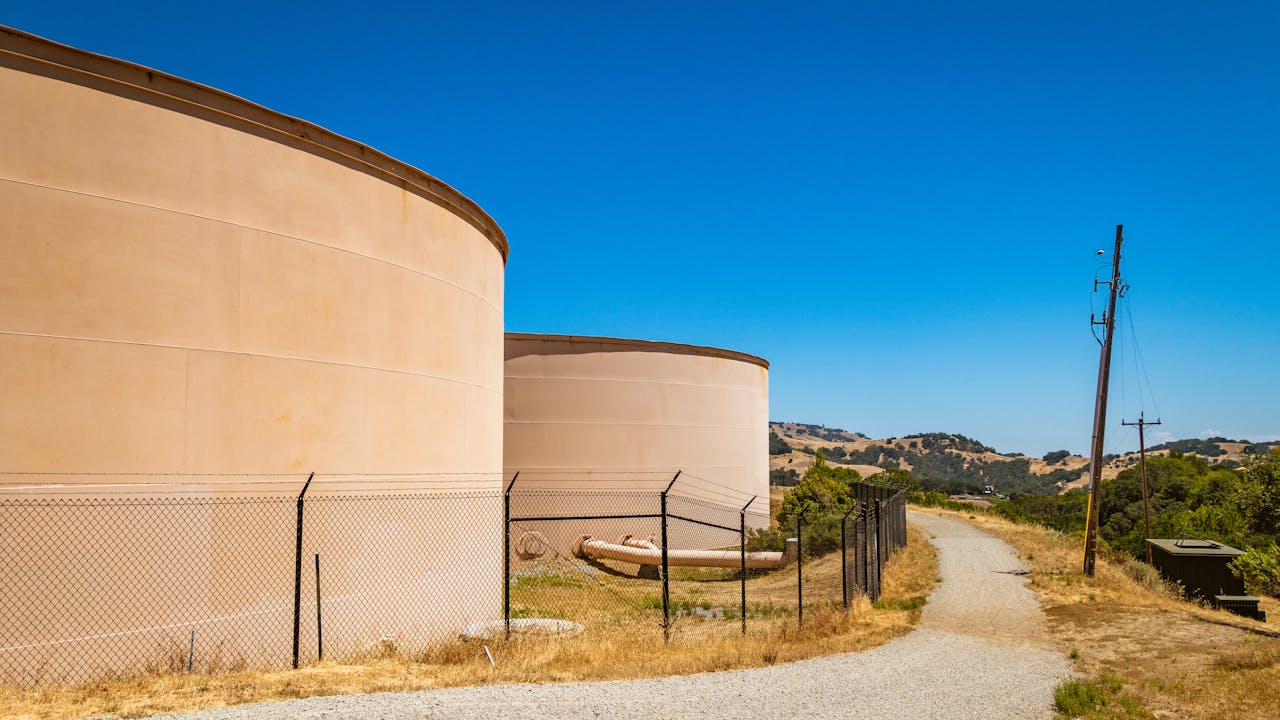 services-03 Large storage tanks in a rural landscape with hills under clear blue skies.